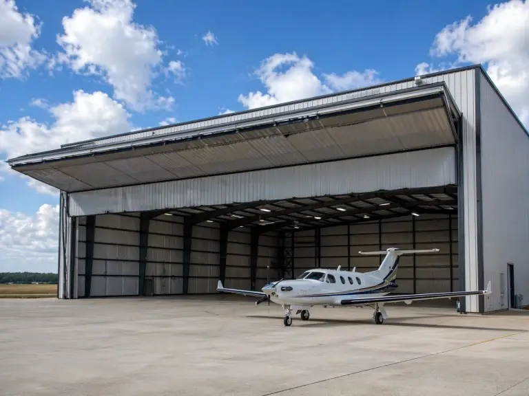 Pre-engineered metal airplane hangar — wide-span aircraft hangar building with hydraulic bifold door and aircraft on apron
