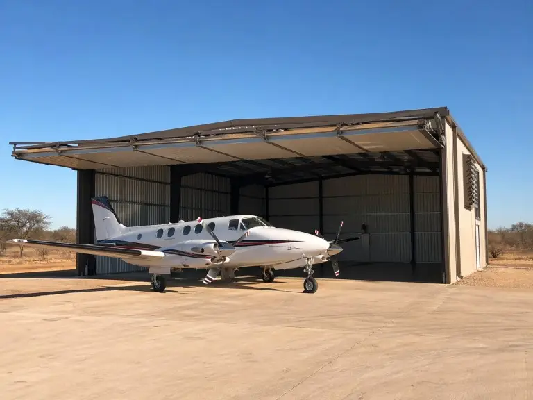 Aircraft hangar building — prefab steel general aviation hangar with hydraulic bifold door at private airfield, Sub-Saharan Africa
