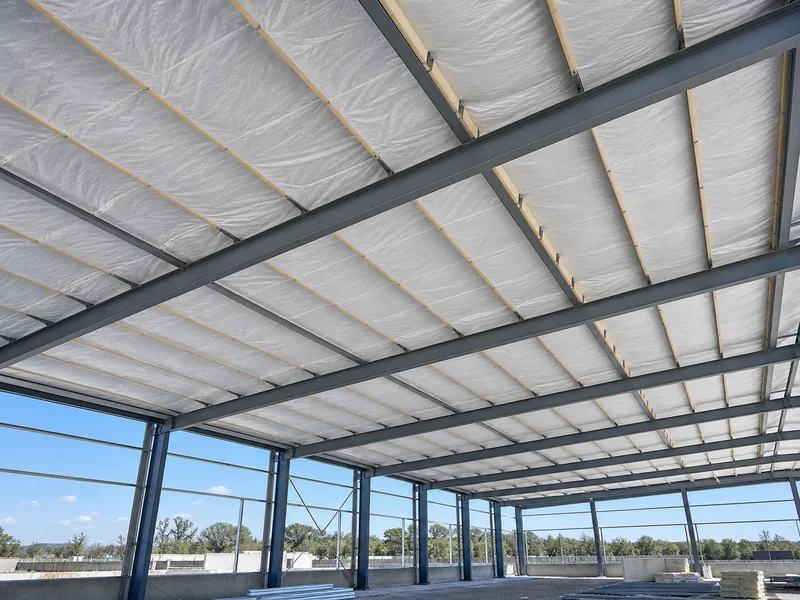 Banded fiberglass blanket and thermal blocks over roof purlins in a metal building